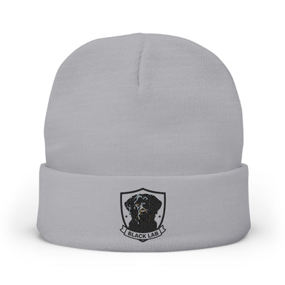 A light gray knit beanie hat with a folded cuff, featuring a black and white graphic of a dog inside a shield with the text 'BLACK LAB' below it.