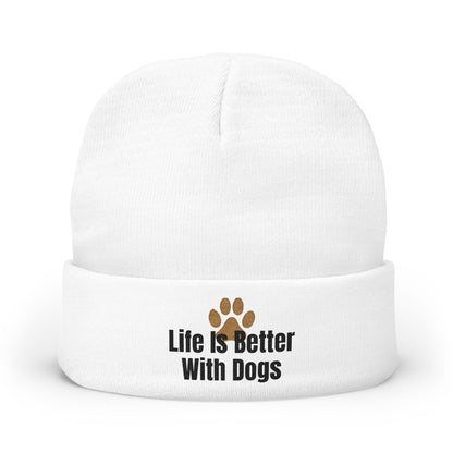 A white knit beanie hat with a folded cuff, featuring the text 'Life Is Better With Dogs' in black next to a brown paw print graphic.