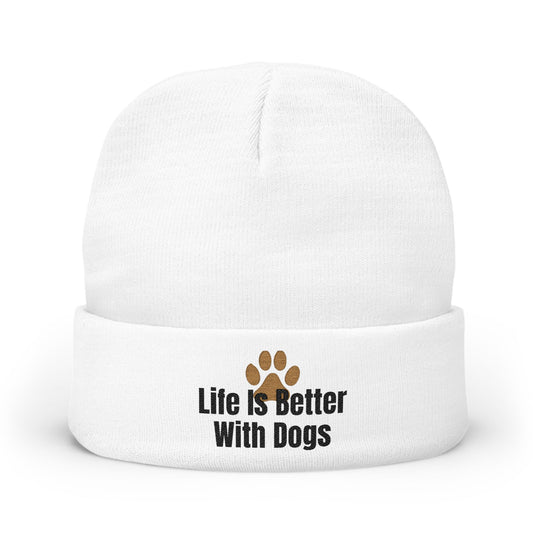 A white knit beanie hat with a folded cuff, featuring the text 'Life Is Better With Dogs' in black next to a brown paw print graphic.