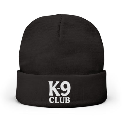 A black knit beanie hat with a folded cuff, featuring the words 'K-9 CLUB' embroidered in white on the front, set against a plain white background.