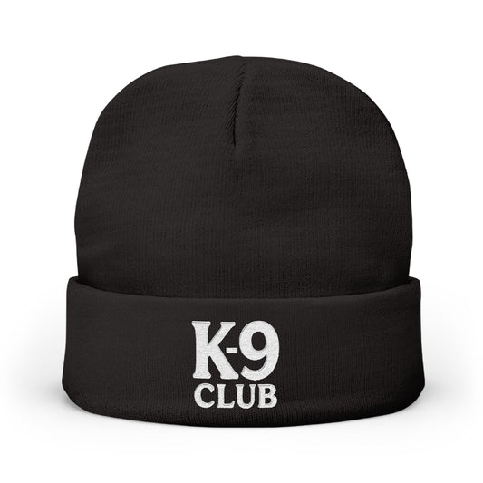 A black knit beanie hat with a folded cuff, featuring the words 'K-9 CLUB' embroidered in white on the front, set against a plain white background.