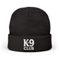 A black knit beanie hat with a folded cuff, featuring the words 'K-9 CLUB' embroidered in white on the front, set against a plain white background.