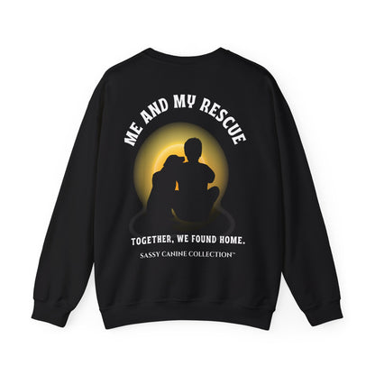 A black crewneck sweatshirt shown from the back, featuring a graphic of a silhouette of a dog and cat sitting together in front of a glowing yellow full moon. White text reads 'ME AND MY RESCUE' above the graphic and 'TOGETHER, WE FOUND HOME.