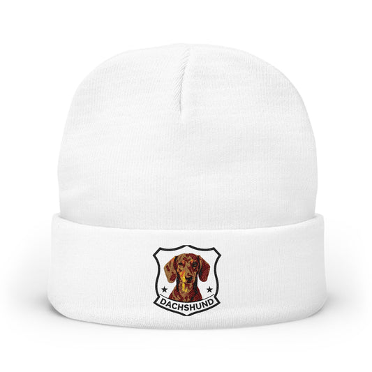 A white knit cuffed beanie hat featuring a shield-shaped Dachshund graphic on the front cuff.