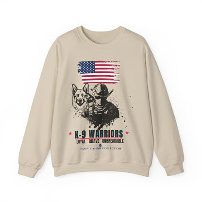 A beige crewneck sweatshirt featuring a graphic print of a German Shepherd, a K-9 officer in a helmet, a distressed American flag, and the text 'K-9 WARRIORS LOYAL BRAVE UNBREAKABLE' with 'SANNI CATHOLIC COLLECTIONT' printed below.