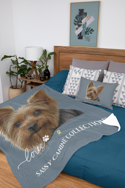 A custom pet blanket and matching pillow set displayed on a bed in a styled bedroom. Each sold separately. The blanket and pillow features a realistic image of a Yorkshire Terrier with the text 'Sassy Canine Collection' and 'Love'.