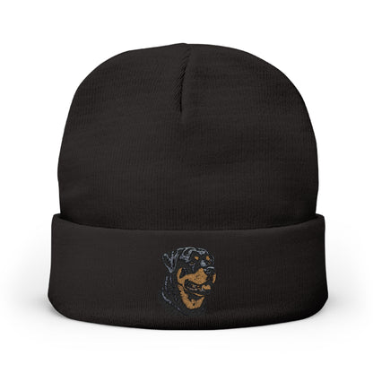 A black knit beanie hat with a folded cuff, featuring a small embroidered graphic of a dog's face in blue and tan on the front cuff, set against a plain white background.

