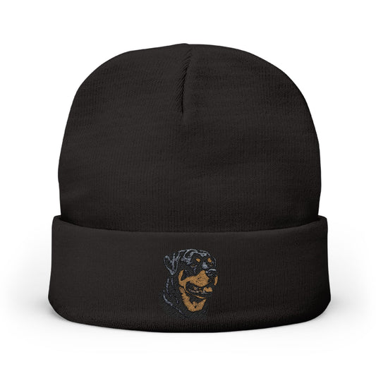 A black knit beanie hat with a folded cuff, featuring a small embroidered graphic of a dog's face in blue and tan on the front cuff, set against a plain white background.

