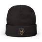 A black knit beanie hat with a folded cuff, featuring a small embroidered graphic of a dog's face in blue and tan on the front cuff, set against a plain white background.

