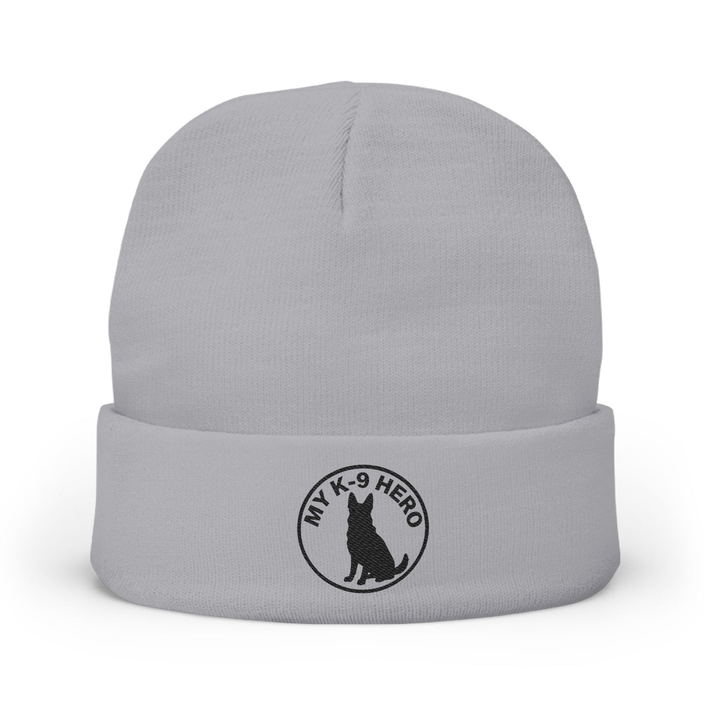 A light gray knit beanie hat with a folded cuff, featuring a black circular embroidered logo on the front that reads 'MY K-9 HERO' around a dog silhouette.