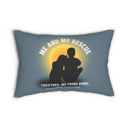 A lumbar throw pillow in slate blue with a printed graphic of a rescue dog and cat silhouette in front of a glowing yellow sun. White text reads 'ME AND MY RESCUE' above the silhouettes and 'TOGETHER, WE FOUND HOME.