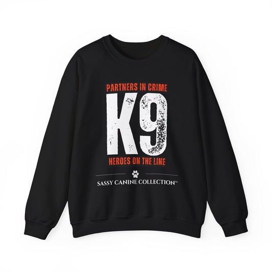 A black crewneck sweatshirt with a distressed graphic print featuring the text 'PARTNERS IN CRIME K9 HEROES ON THE LINE' in orange and white, and 'SASSY CANINE COLLECTION' at the bottom.