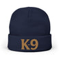 A navy blue knit beanie with a folded cuff featuring the text 'K-9' embroidered in a tan/gold color, shown against a plain white background.