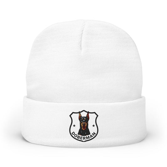A white knit cuffed beanie hat featuring a printed Doberman dog crest logo on the front cuff.