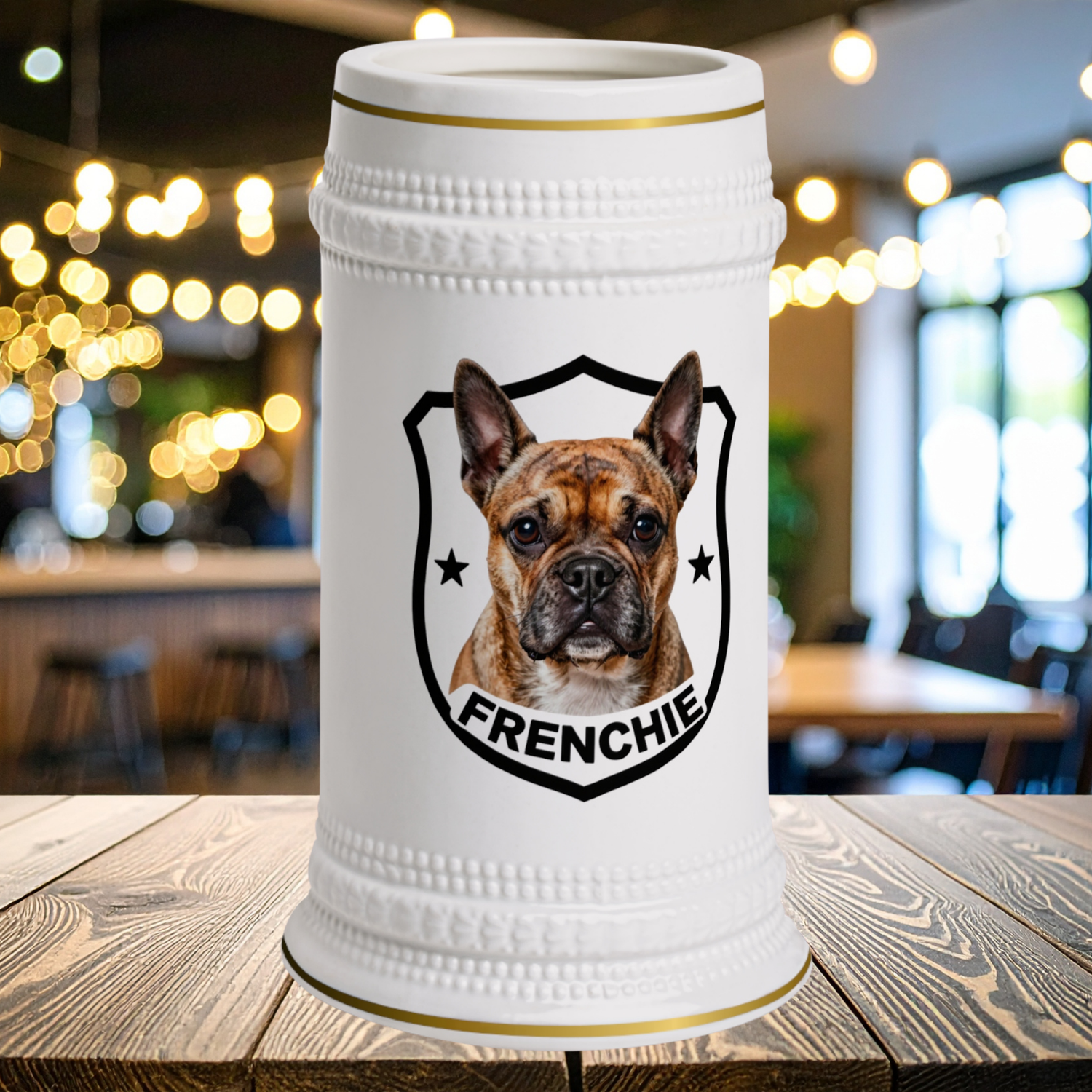 A white ceramic beer stein with gold trim sits features a French Bulldog inside a black shield outline with the word 'FRENCHIE' below it.