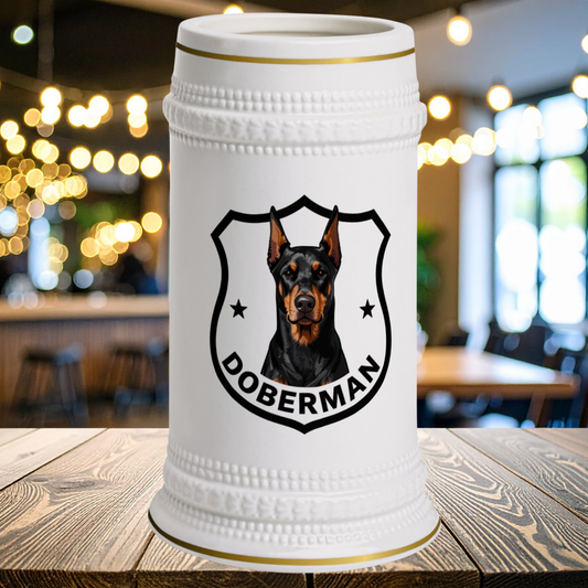 A white ceramic beer stein with a gold-trimmed rim and base, featuring a black and brown Doberman dog portrait in a shield with the word DOBERMAN