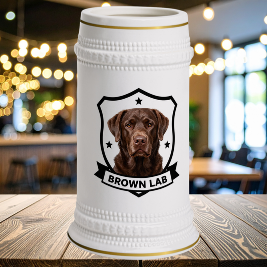 A white ceramic beer stein with gold trim  features a portrait of a brown Labrador retriever inside a black shield outline with the text 'BROWN LAB