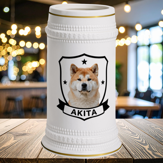 A white ceramic beer stein with a gold-trimmed rim and base, featuring a  shield emblem with an Akita dog portrait and the word 'AKITA' on a banner