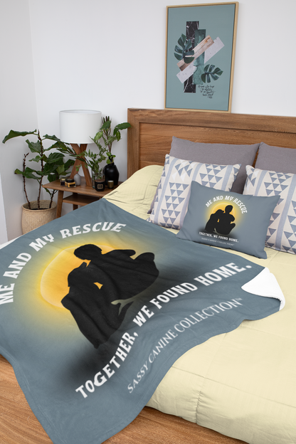 A dog rescue-themed bedding set displayed on a bed in a styled bedroom. The set includes a large slate blue blanket and matching pillows featuring a silhouette of a dog and a person sitting together in front of a yellow sun, with the text 'ME AND MY RESCUE TOGETHER, WE FOUND HOME.